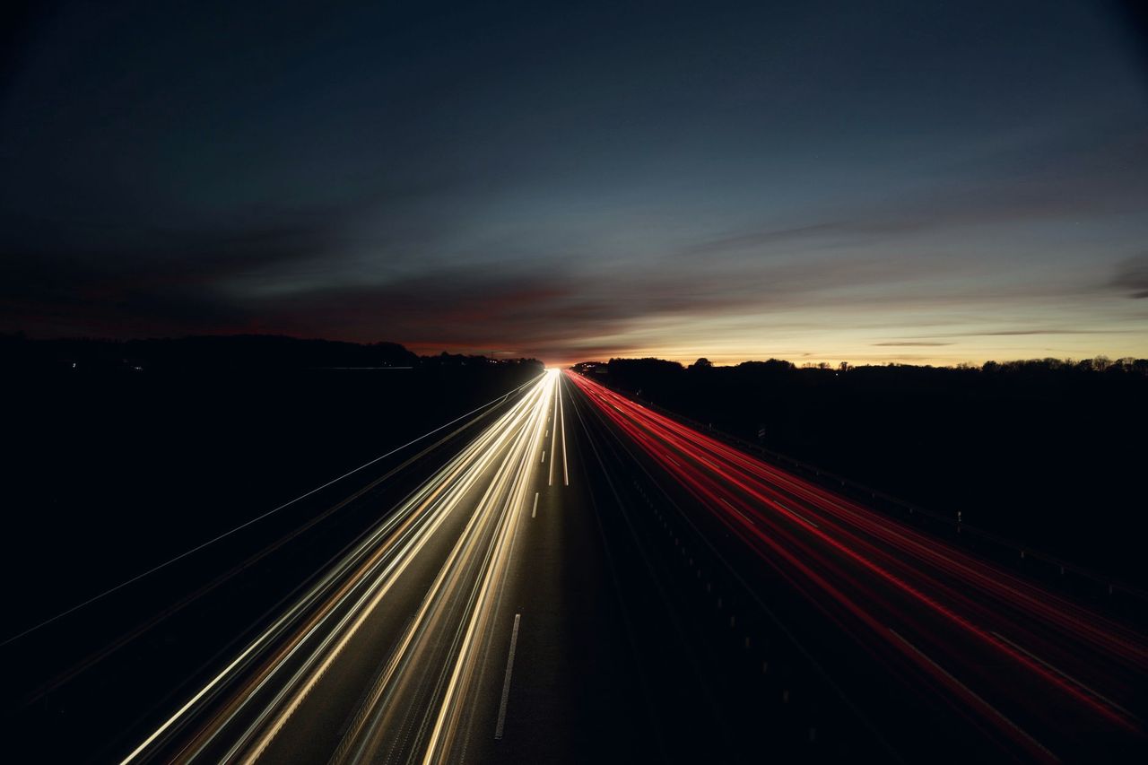 Traînées de phares blanches et rouges sur une autoroute sous un ciel de crépuscule